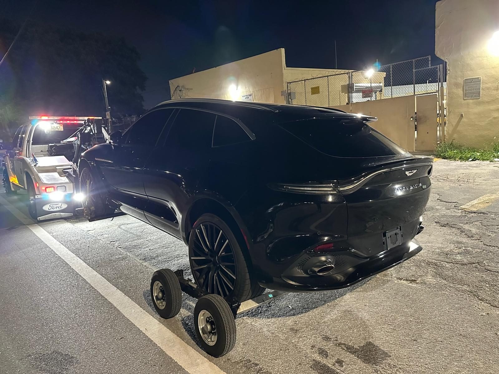 Black Aston Martin DBX photographed at night with the tow truck lights behind it before being hooked up