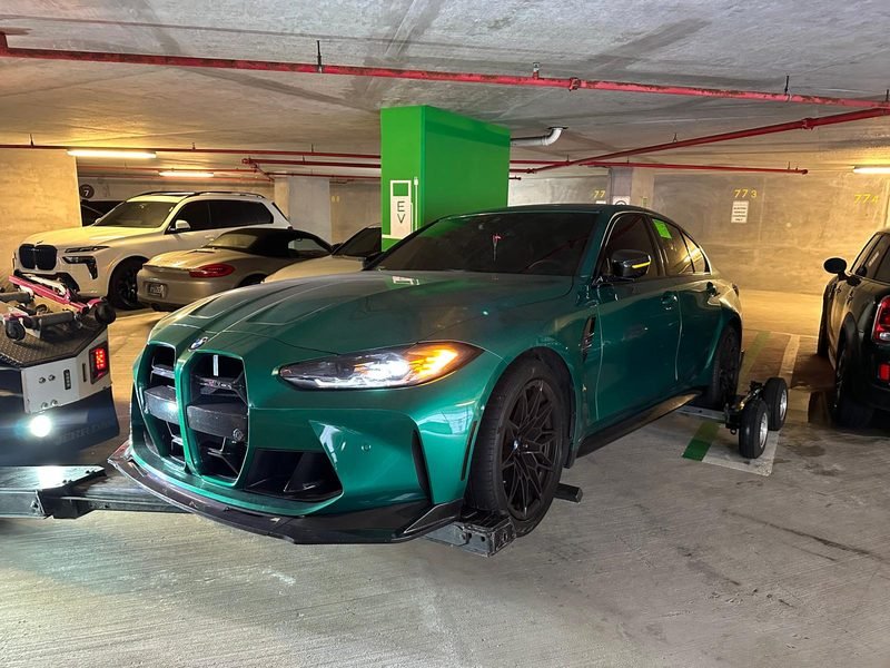 Green BMW M3 Competition being loaded onto a flatbed inside an underground parking garage