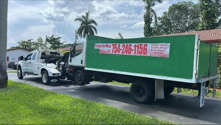 Green medium-duty box truck hooked to the white wrecker on a residential street