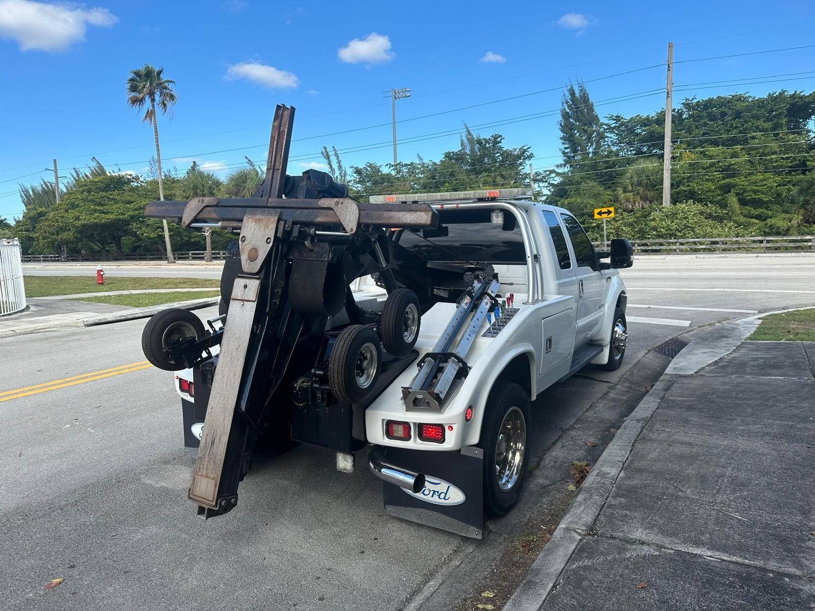 White Ford F-450 wrecker parked roadside in Miami with its boom raised and wheel-lift extended
